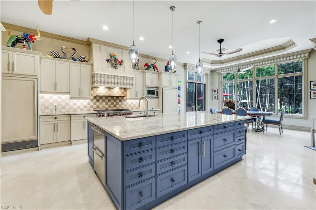 Kitchen with a ceiling fan, hanging light fixtures, ornamental molding, light stone counters, and a raised ceiling