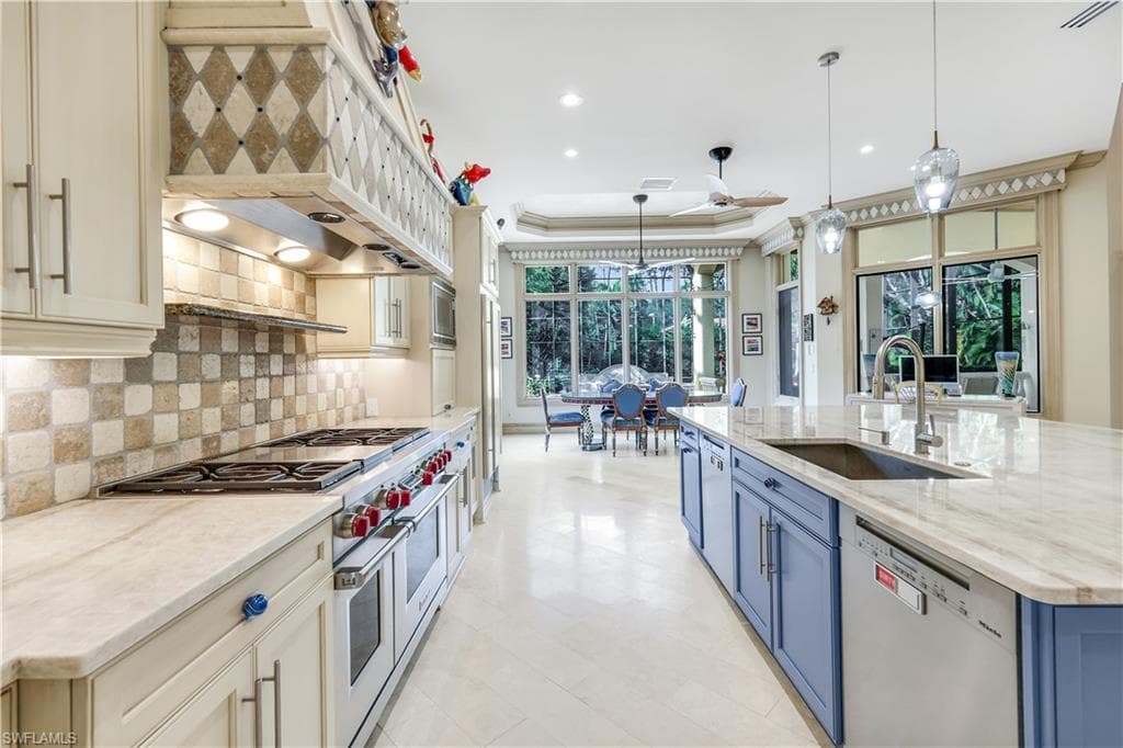 Kitchen with hanging light fixtures, appliances with stainless steel finishes, light stone countertops, custom exhaust hood, and blue cabinetry
