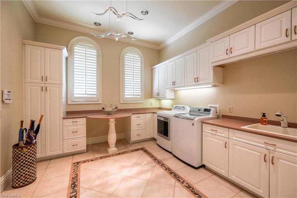 Main Laundry Room with white cabinetry, light tile patterned floors, inlaid floor details, ornamental molding, and separate washer and dryer