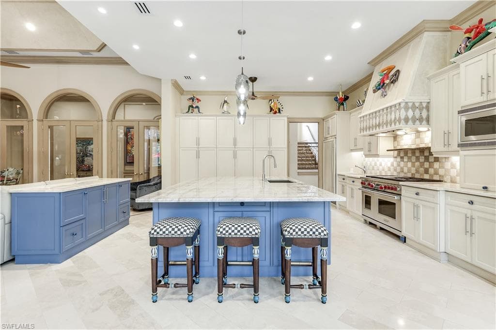 Kitchen with blue cabinets, hanging light fixtures, light stone countertops, crown molding, and stainless steel appliances