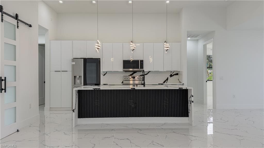 Kitchen with a barn door, modern cabinets, pendant lighting, white cabinetry, and a towering ceiling