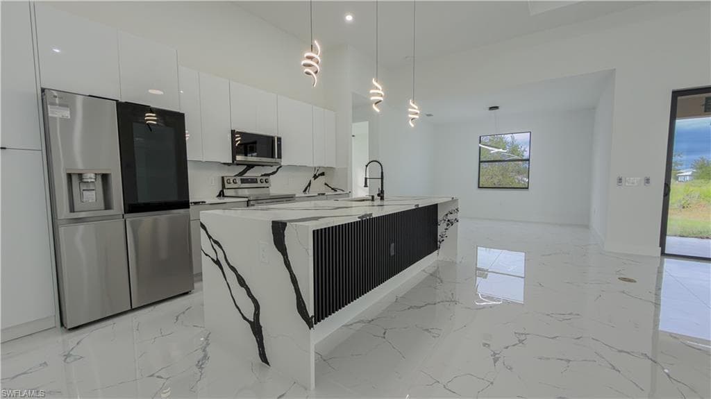 Kitchen with stainless steel appliances, decorative light fixtures, light marble finish floors, modern cabinets, and light stone countertops