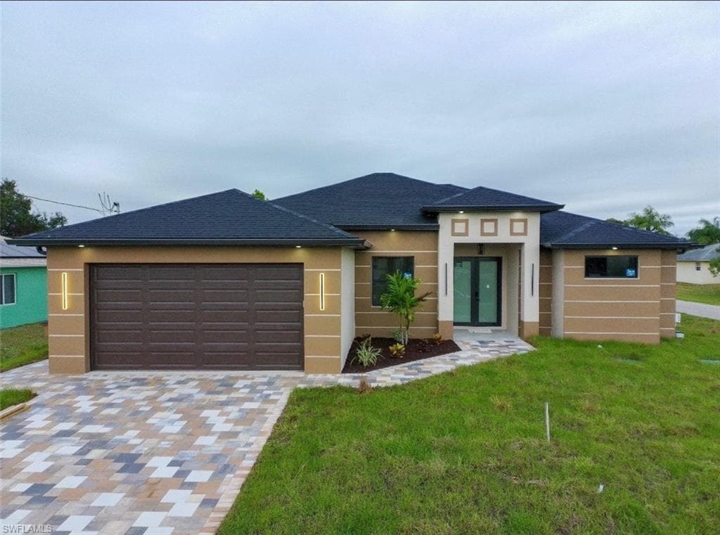 Prairie-style home with decorative driveway, an attached garage, a front yard, and stucco siding