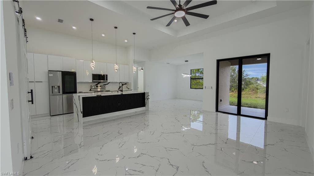 Unfurnished living room featuring a high ceiling, light marble finish flooring, recessed lighting, ceiling fan, and a tray ceiling