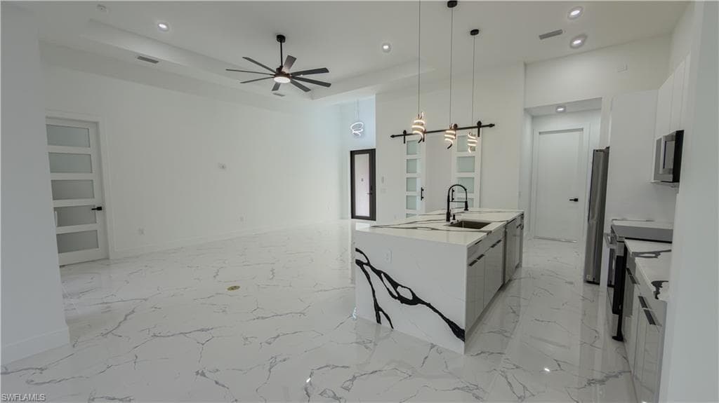 Kitchen featuring recessed lighting, light marble finish flooring, pendant lighting, a center island with sink, and stainless steel appliances