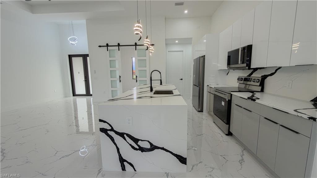 Kitchen featuring modern cabinets, appliances with stainless steel finishes, a barn door, decorative light fixtures, and a high ceiling