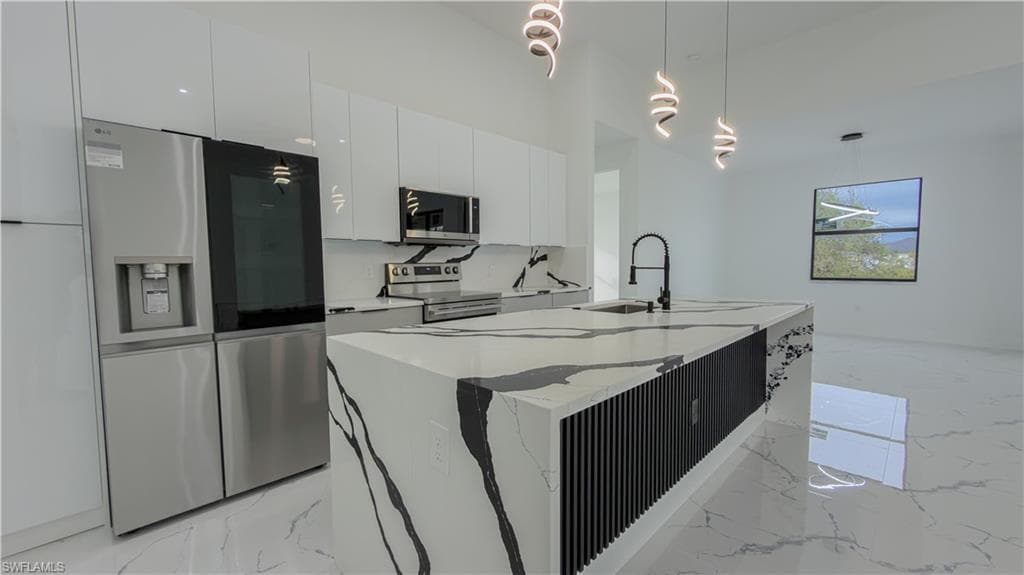 Kitchen with appliances with stainless steel finishes, modern cabinets, decorative light fixtures, white cabinetry, and light stone countertops