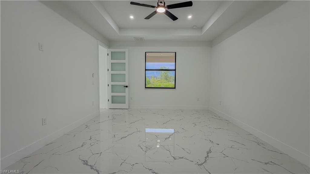 Empty room featuring a tray ceiling, recessed lighting, light marble finish floors, and ceiling fan