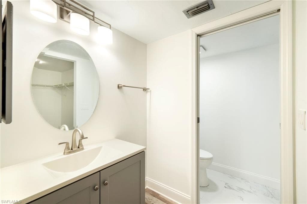 Bathroom with vanity, light marble finish floors, and a walk in closet