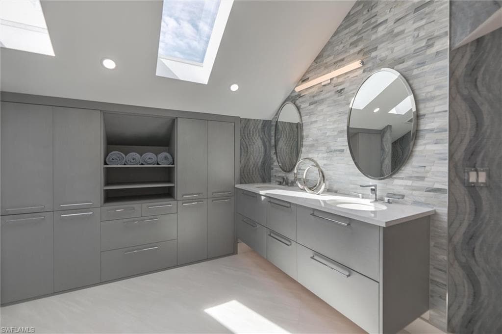 Bathroom featuring double sink vanity, backsplash, and lofted ceiling with skylight