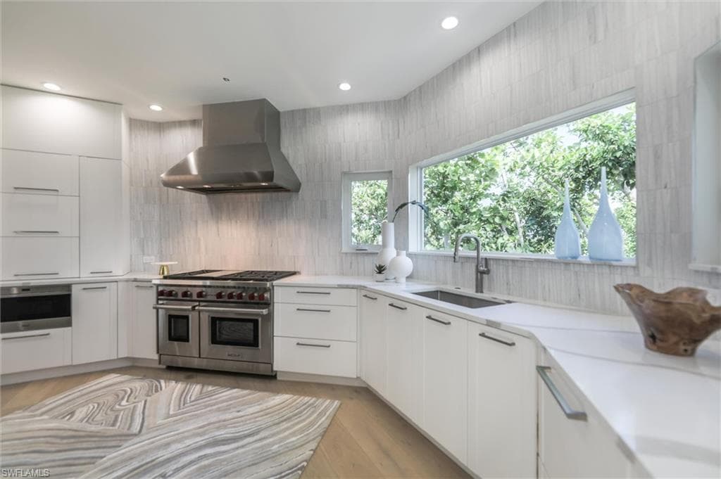 Kitchen featuring light hardwood / wood-style flooring, sink, wall chimney exhaust hood, white cabinetry, and appliances with stainless steel finishes