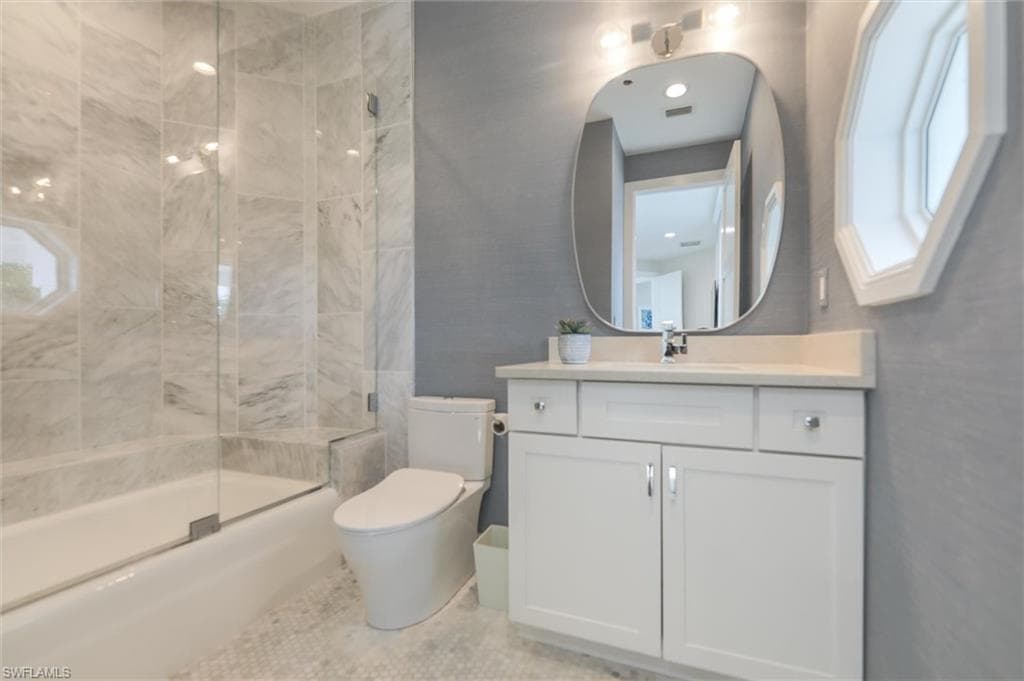 Full bathroom featuring enclosed tub / shower combo, vanity, and toilet
