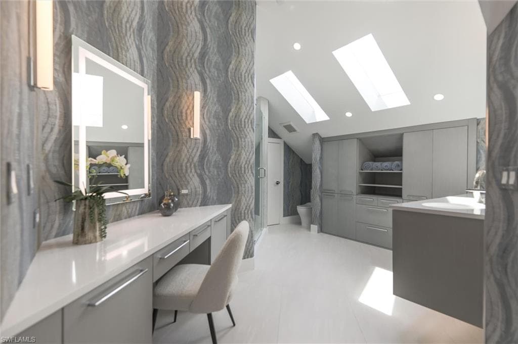 Bathroom featuring tile floors, vaulted ceiling with skylight, toilet, and vanity
