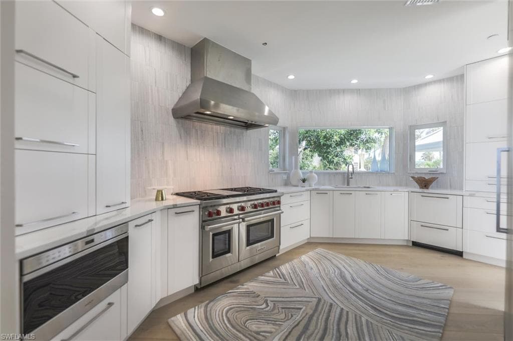 Kitchen with range with two ovens, oven, wall chimney range hood, sink, and white cabinetry