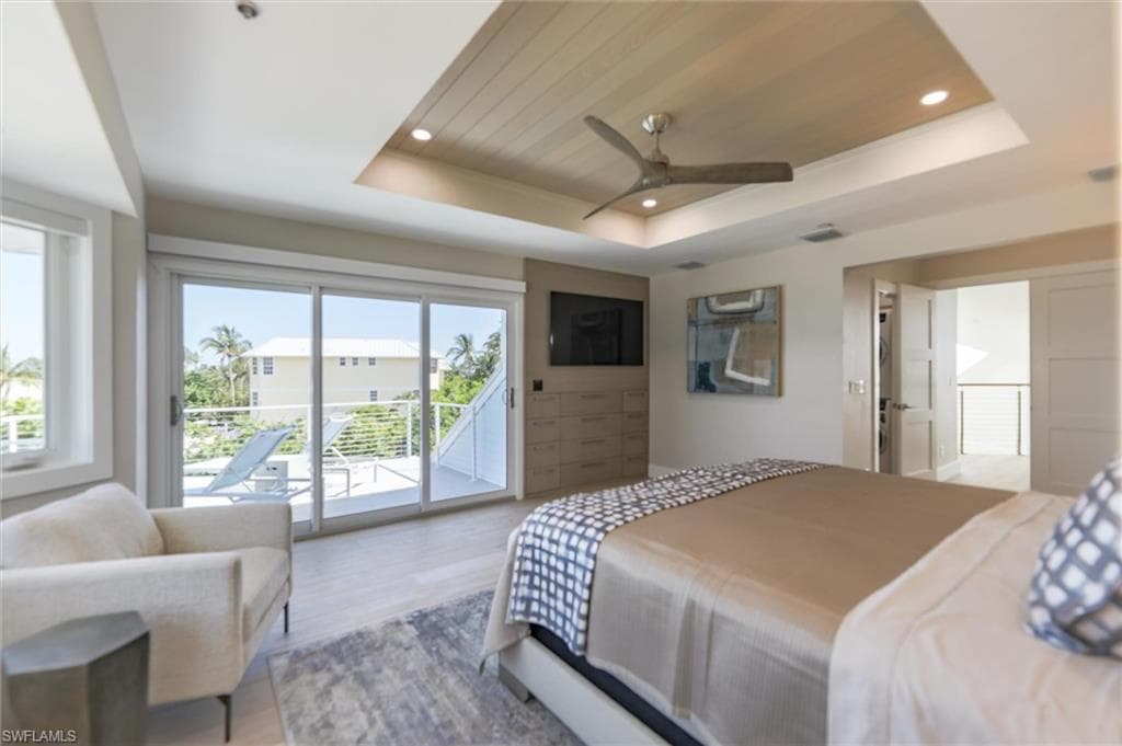 Bedroom with ceiling fan, a raised ceiling, light wood-type flooring, and access to outside