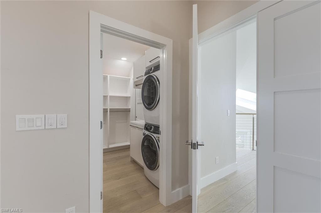 Washroom with light hardwood / wood-style flooring and stacked washing maching and dryer