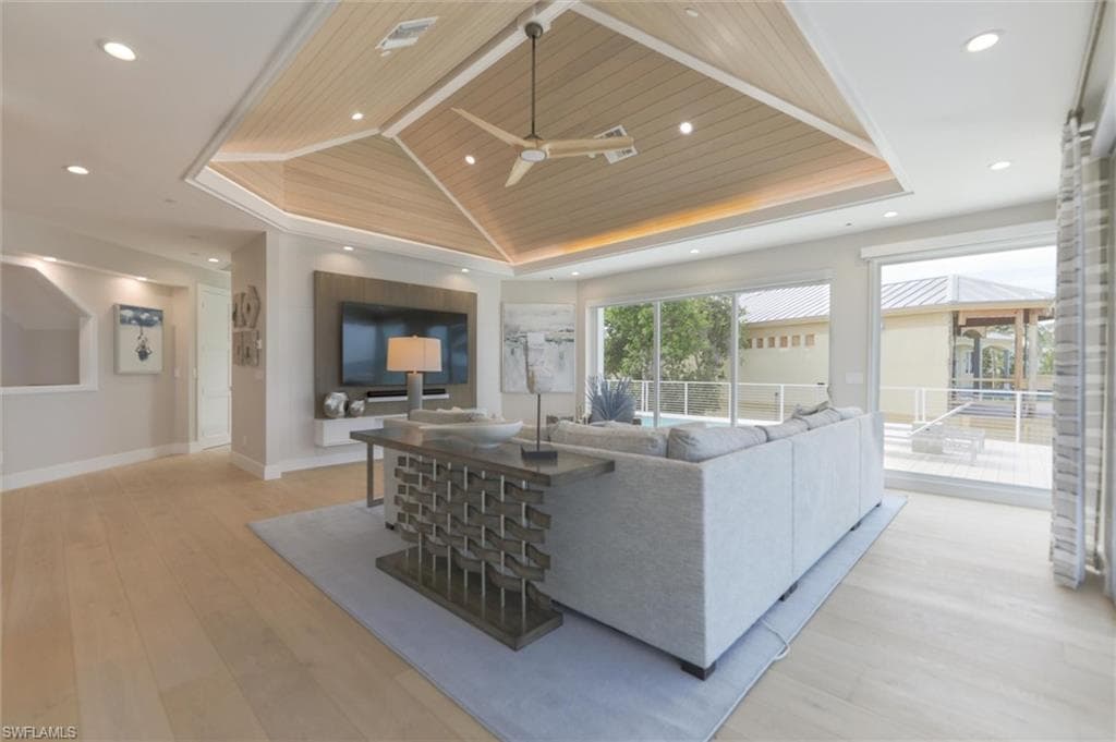 Living room with ceiling fan, a raised ceiling, light wood-type flooring, and wooden ceiling