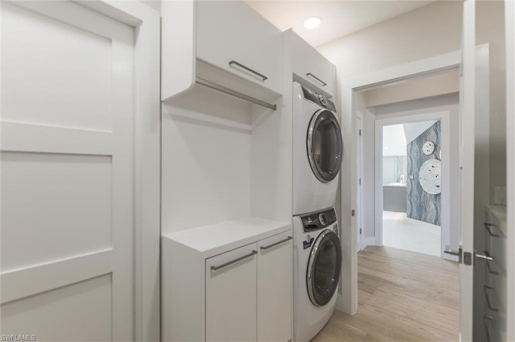 Clothes washing area with stacked washer and clothes dryer, light wood-type flooring, and cabinets