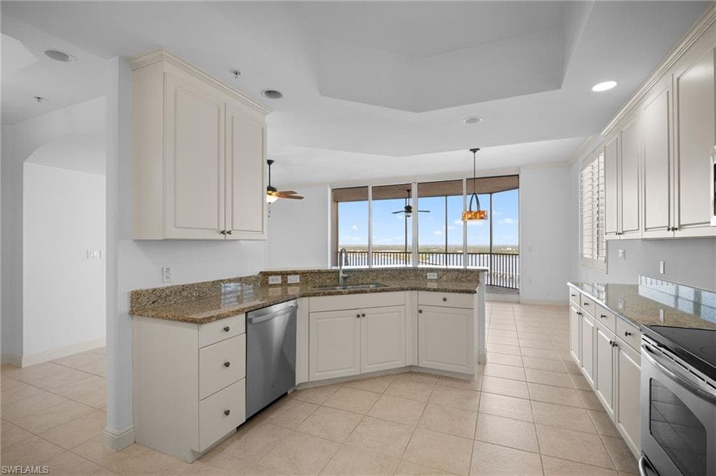Kitchen featuring dark stone countertops, a peninsula, appliances with stainless steel finishes, recessed lighting, and a tray ceiling