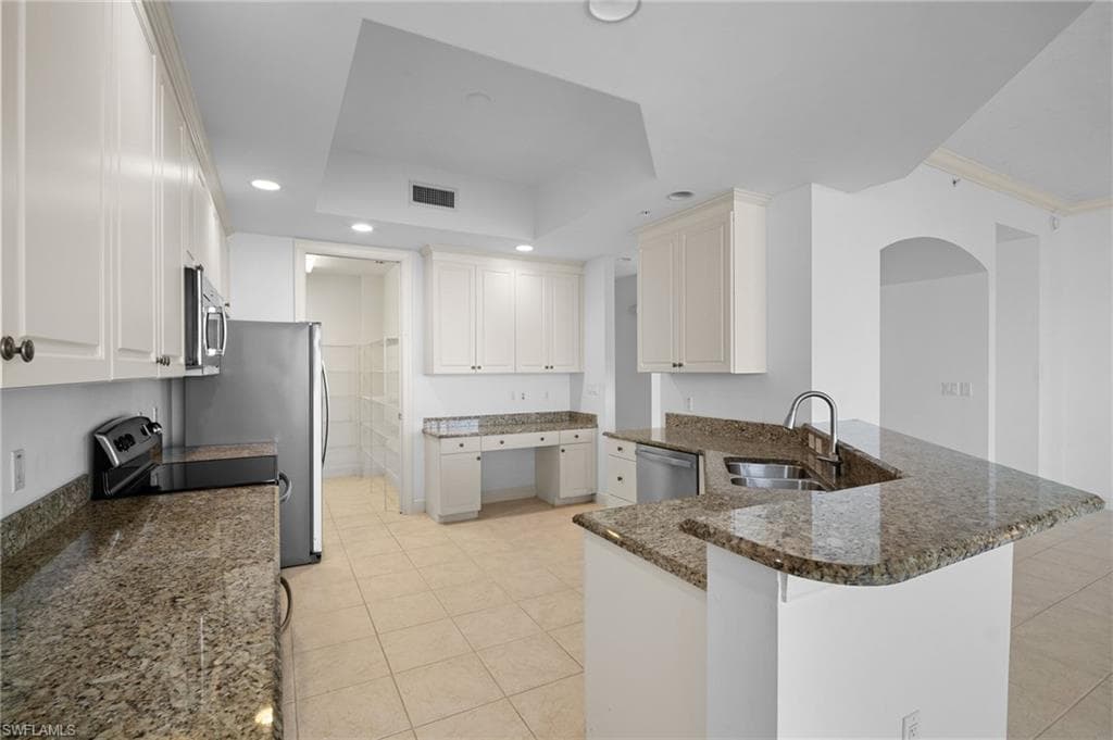 Kitchen featuring dark stone countertops, a peninsula, a raised ceiling, light tile patterned floors, and recessed lighting