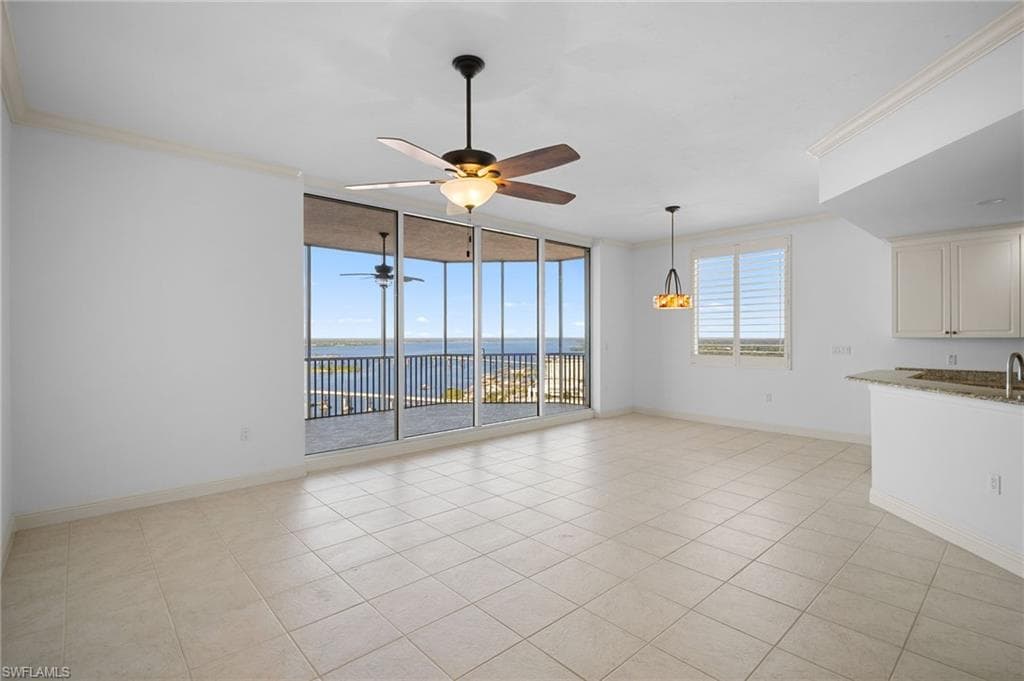 Empty room featuring floor to ceiling windows, ornamental molding, a ceiling fan, light tile patterned floors, and a chandelier