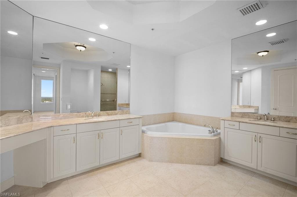 Bathroom with a tray ceiling, a shower stall, recessed lighting, two vanities, and a garden tub