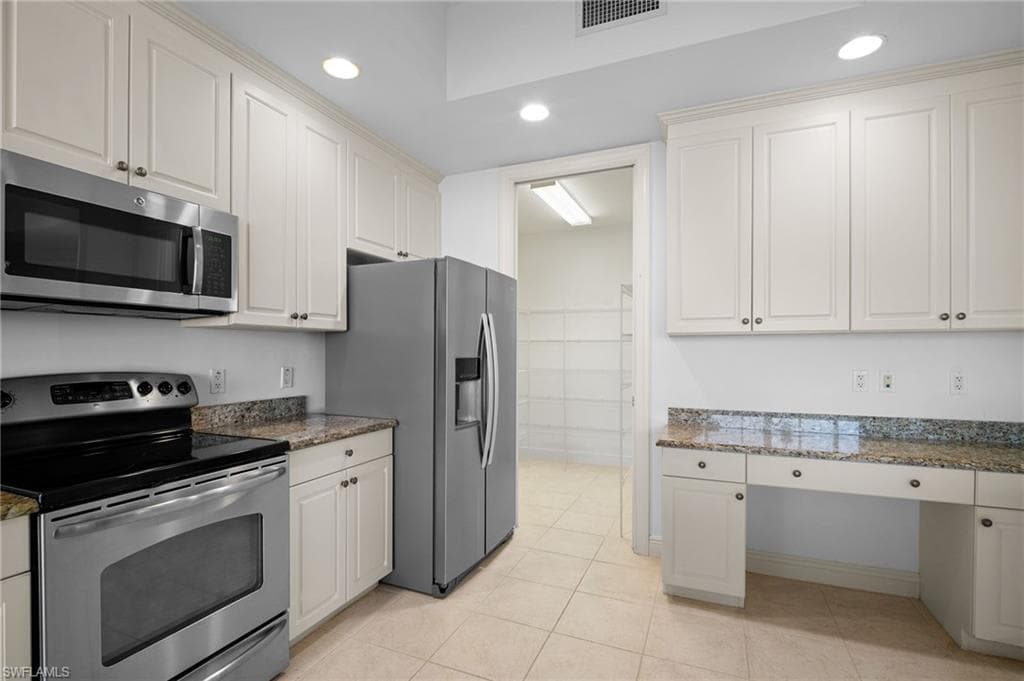 Kitchen featuring stainless steel appliances, built in study area, dark stone countertops, light tile patterned floors, and recessed lighting
