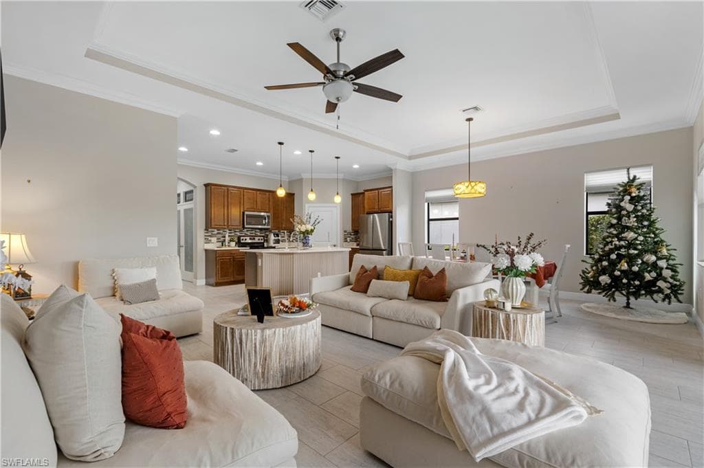 Living area with a tray ceiling, ornamental molding, a ceiling fan, arched walkways, and recessed lighting