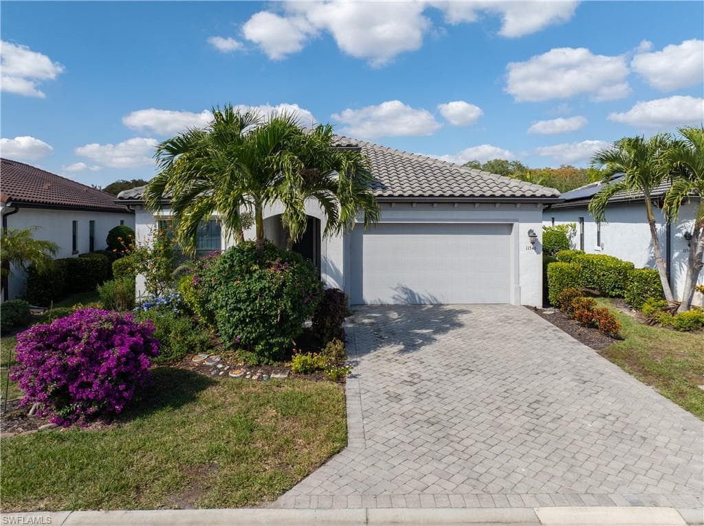 View of front facade featuring a tile roof, decorative driveway, stucco siding, and a garage