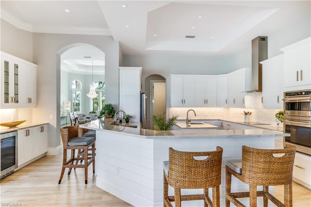 Kitchen with a kitchen bar, arched walkways, white cabinetry, and ornamental molding