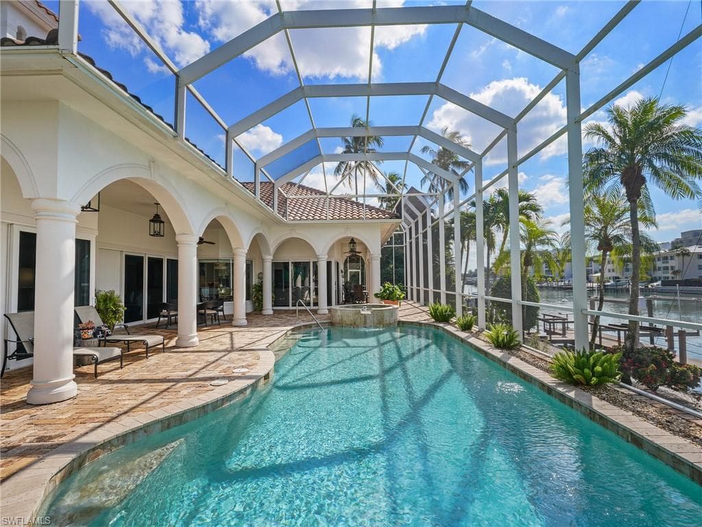 View of pool featuring a sunroom, a patio area, glass enclosure, a pool with connected hot tub, and a water view