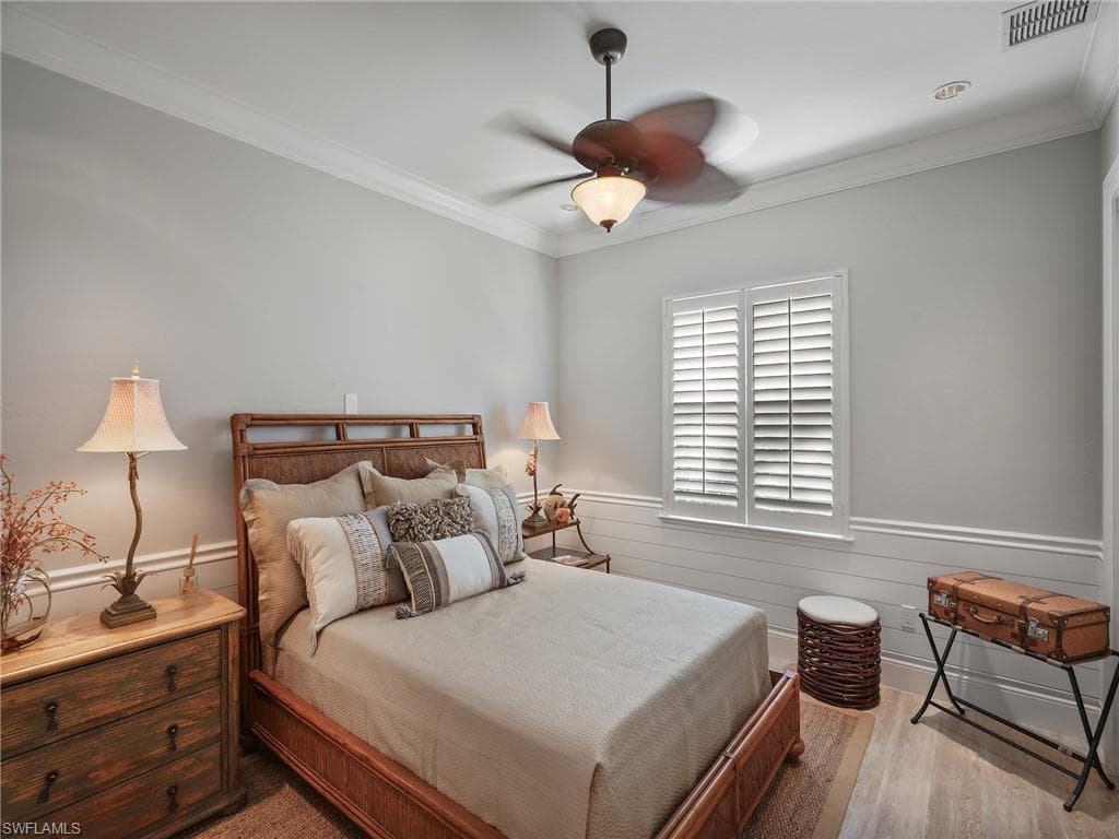Bedroom with wainscoting, ornamental molding, ceiling fan, and light wood-style flooring