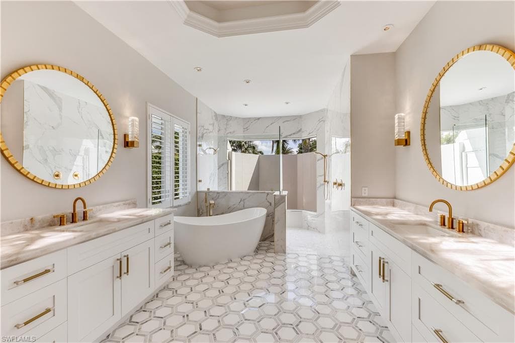 Full bathroom featuring two vanities, a marble finish shower, a freestanding tub, and a tray ceiling