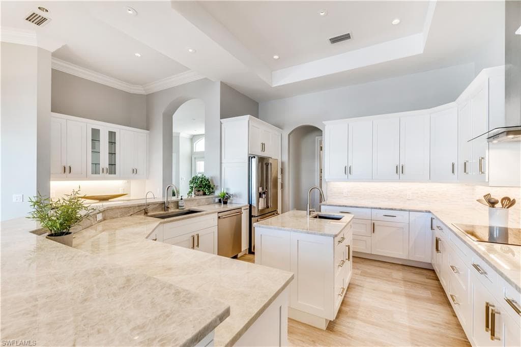 Kitchen featuring an island with sink, white cabinets, light stone countertops, glass insert cabinets, and wall chimney exhaust hood