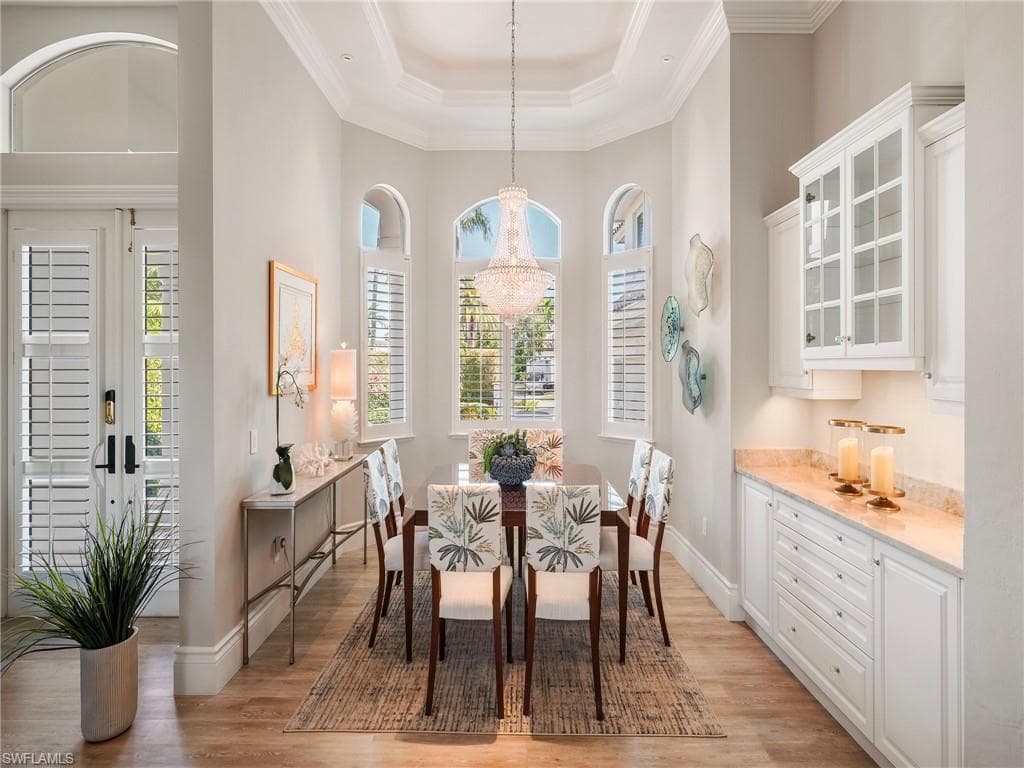 Dining room with a raised ceiling, crown molding, light wood finished floors, a high ceiling, and a chandelier