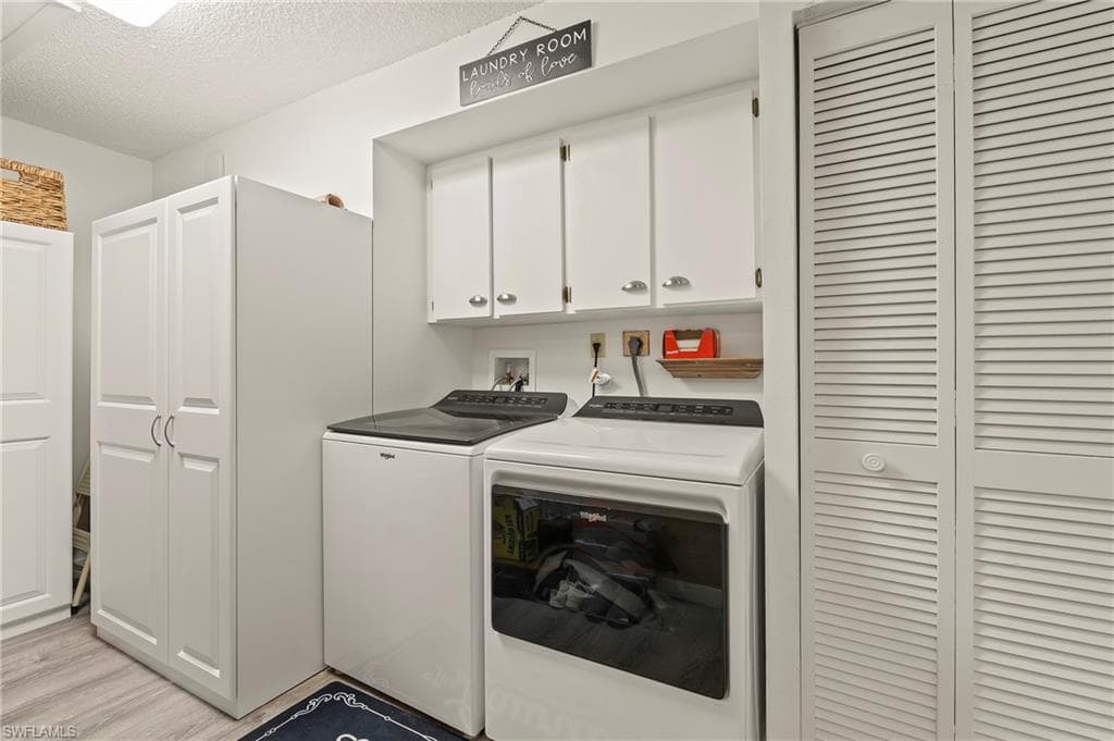 Laundry room with cabinet space, washing machine and clothes dryer, a textured ceiling, and light wood-style flooring