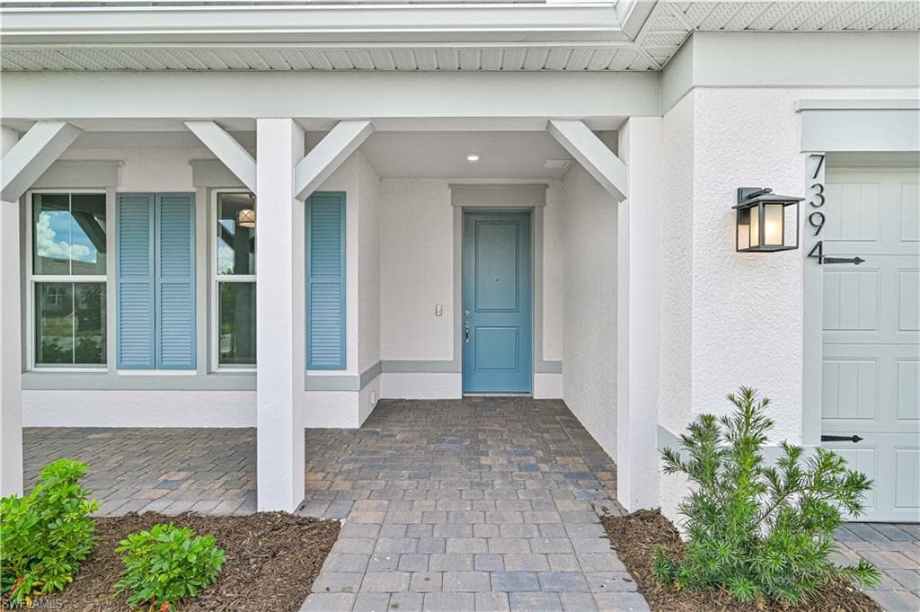 Entrance to property with covered porch, stucco siding, and a garage