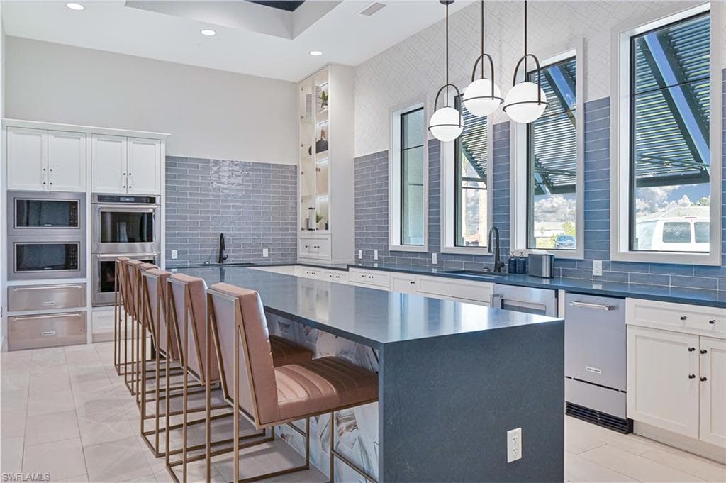 Kitchen with a kitchen breakfast bar, a spacious island, pendant lighting, white cabinets, and stainless steel appliances
