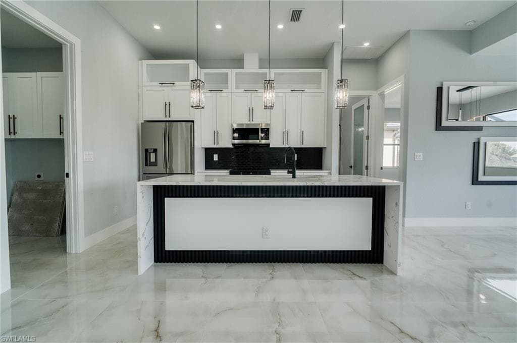 Kitchen featuring white cabinetry, appliances with stainless steel finishes, a kitchen island with sink, light stone countertops, and recessed lighting