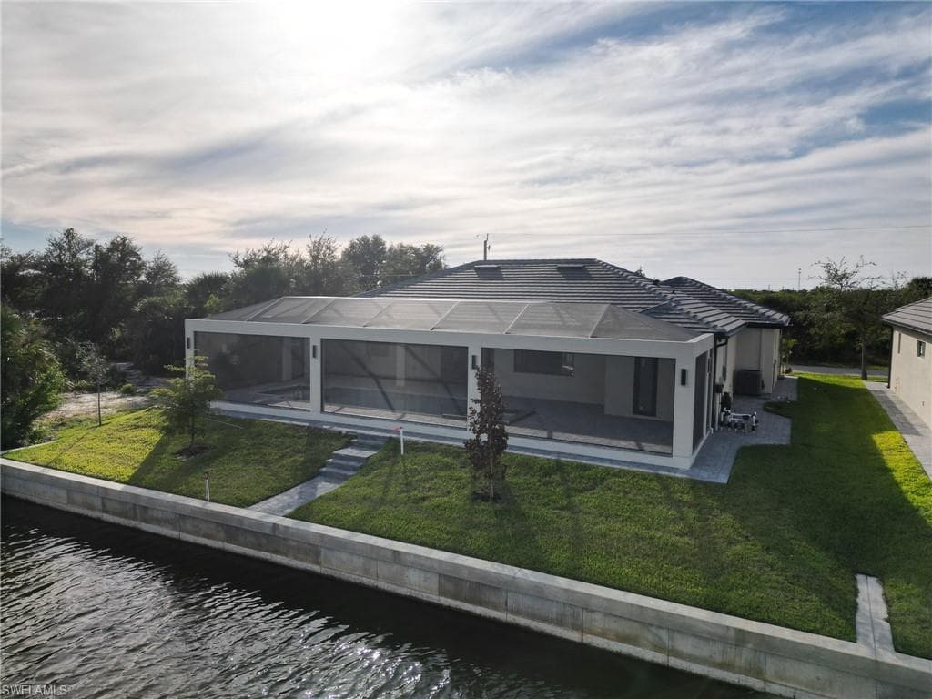 Back of property with a lanai, a lawn, a sunroom, a water view, and an outdoor pool