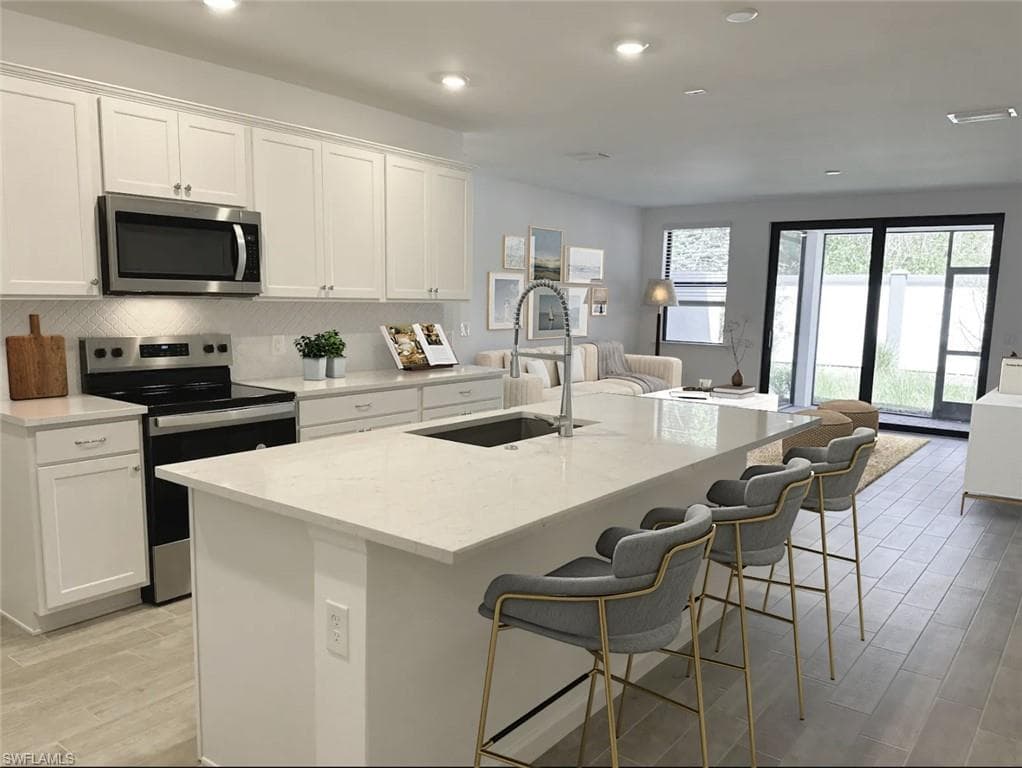 Virtually staged kitchen with appliances with stainless steel finishes, backsplash, wood tiled floors, light stone countertops, and white cabinetry