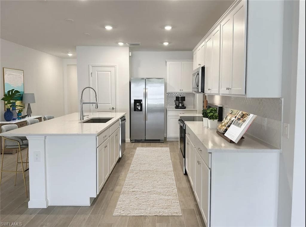 Virtually staged kitchen featuring stainless steel appliances, white cabinetry, light stone countertops, light wood-style flooring, and backsplash