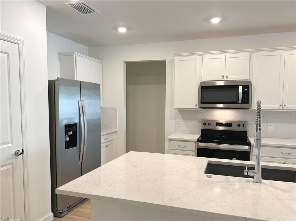 Kitchen with stainless steel appliances, white cabinets, light stone countertops, tasteful backsplash, and light wood-style floors