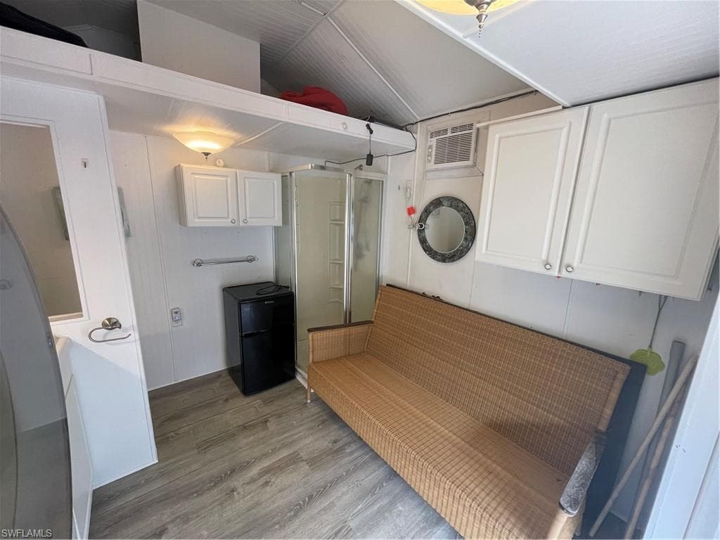 Kitchen featuring white cabinetry, light wood-style floors, fridge, lofted ceiling, and a wall mounted AC