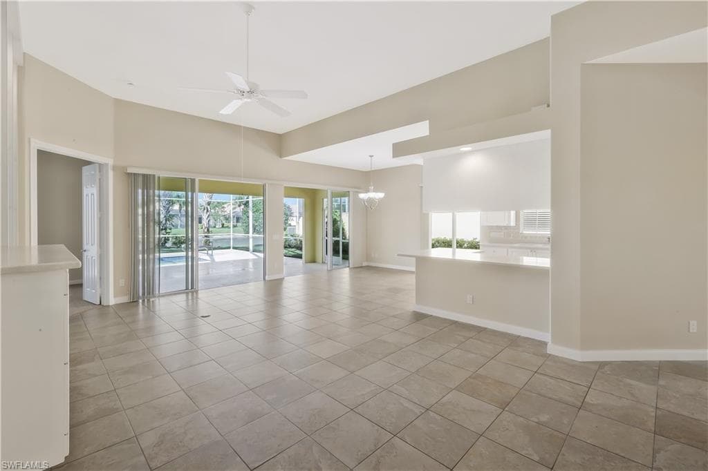 Empty room featuring a ceiling fan, light tile patterned floors, a chandelier, and a towering ceiling