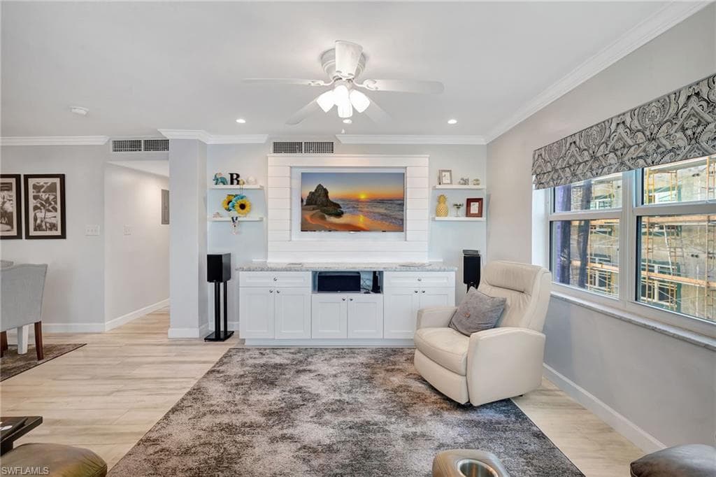 Living room has custom enertainment center, light wood-like tile flooring, ceiling fan and recessed lighting