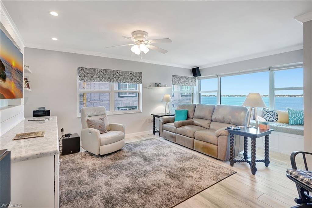 Living room with river view, crown molding, wood-like tile floor, impact windows.