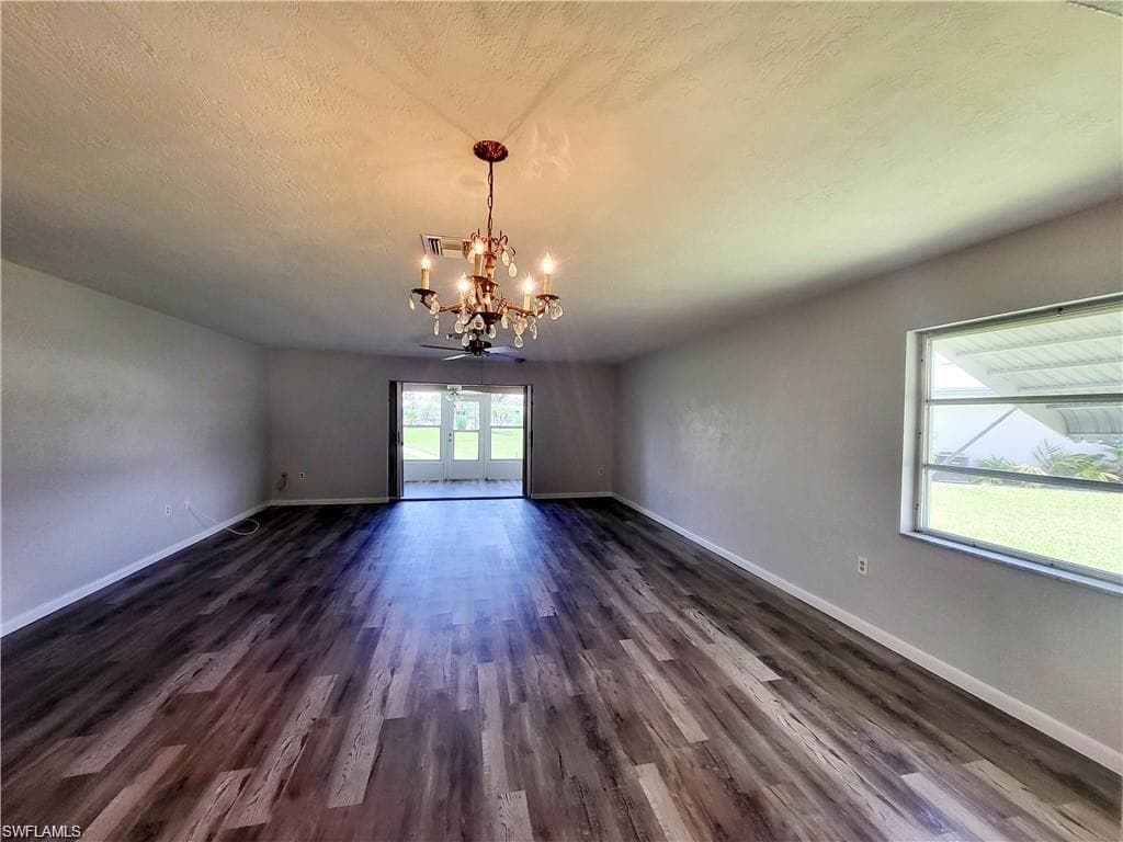 Spare room featuring dark wood-type flooring, a chandelier, and a textured ceiling