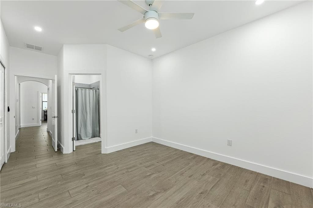 Empty room featuring light wood-style floors, arched walkways, recessed lighting, and a ceiling fan