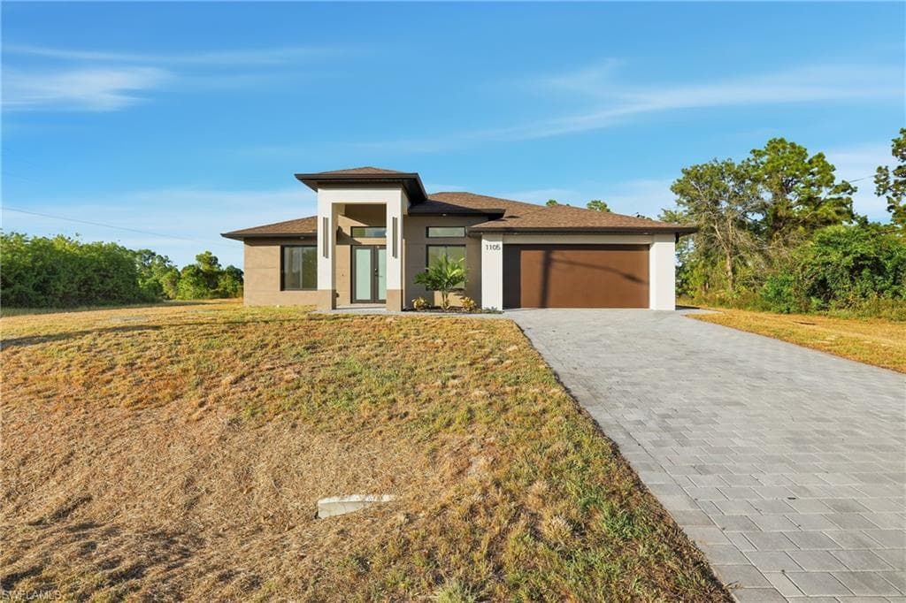 Prairie-style house featuring a garage, decorative driveway, stucco siding, and a front yard